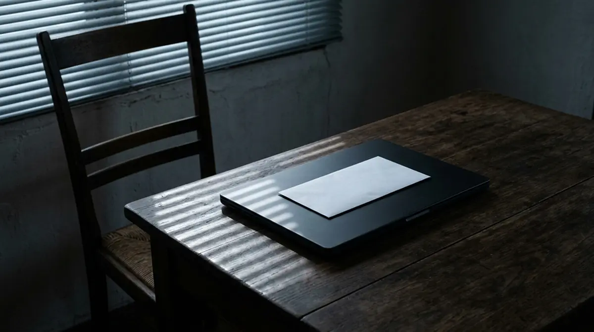Leerer Schreibtisch mit geschlossenem Notebook und einem unbeschrifteten Briefumschlag ohne Absender
